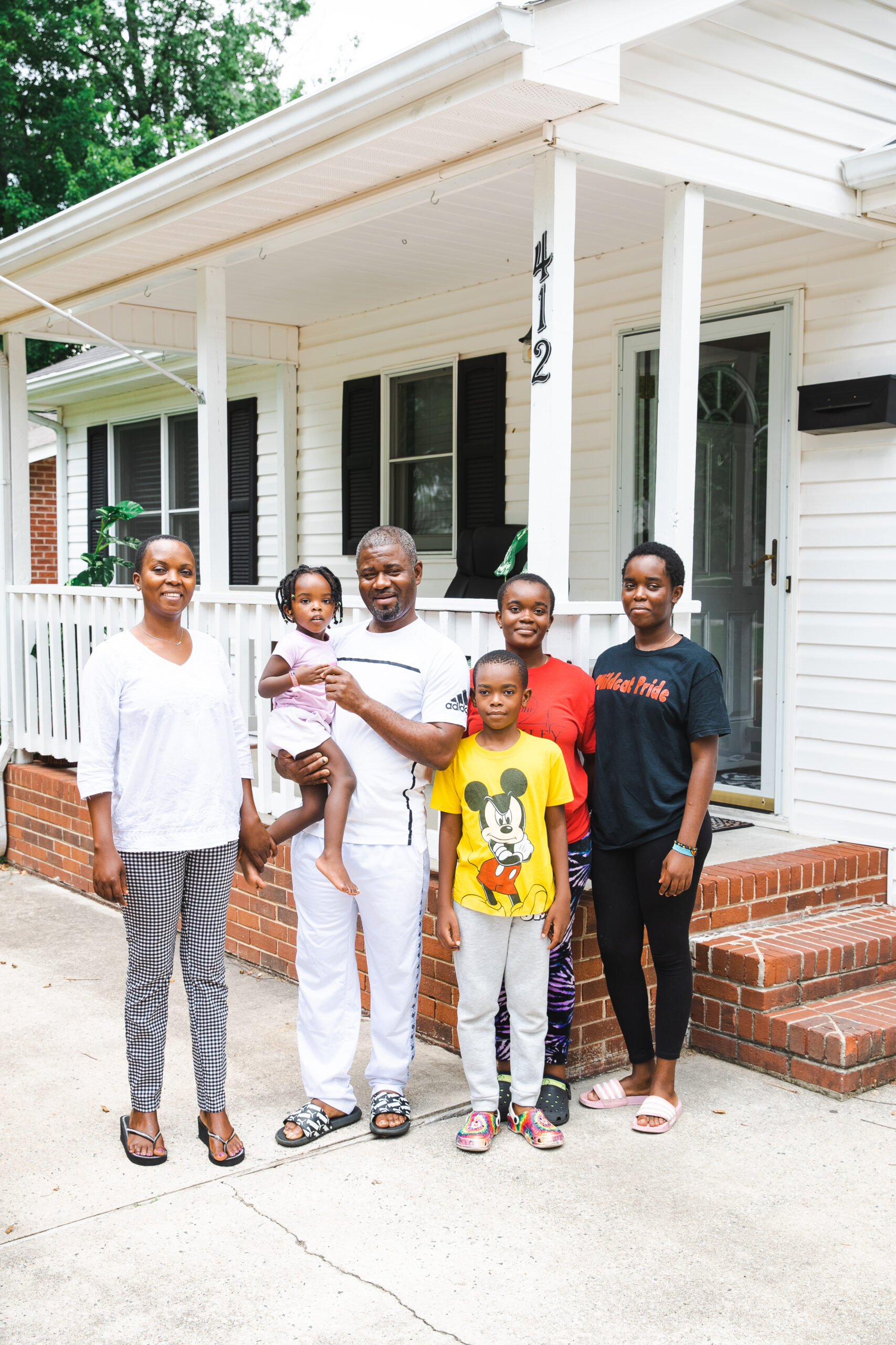 The Lwambas stand in front of their home in High Point, NC with their children, ranging in ages from 16 to two and a half.